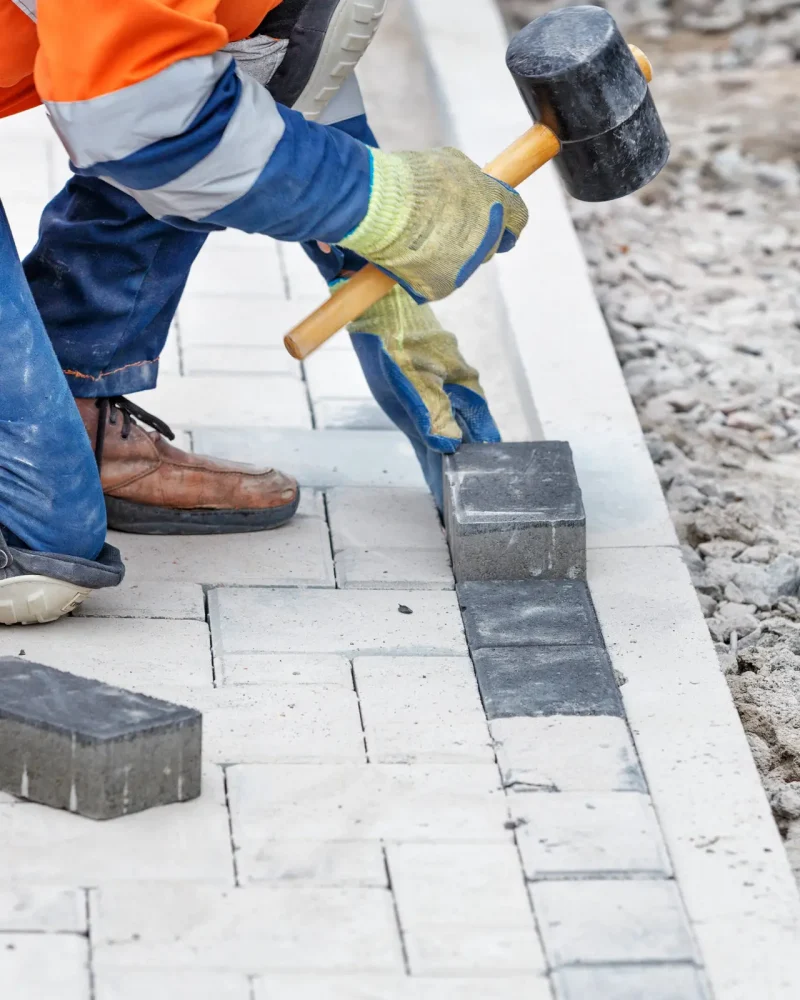 A vertical closeup of the worker banging the paving slabs with a rubber mallet.