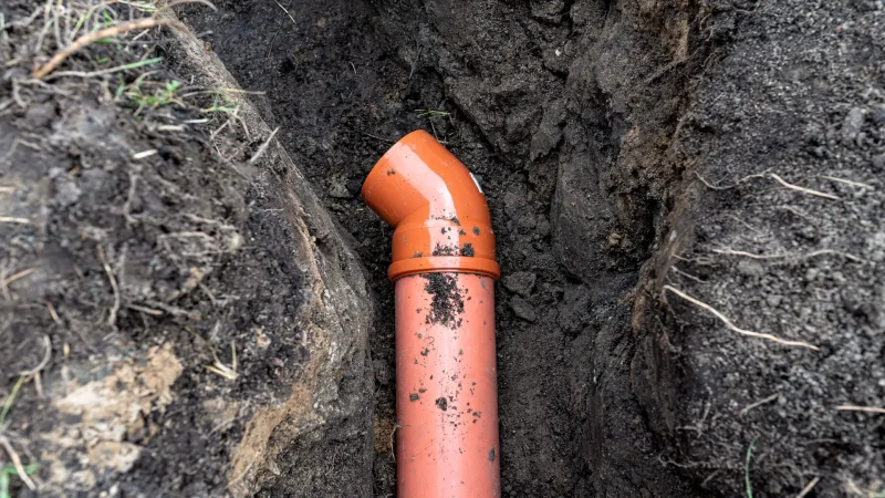 An orange plastic pipe from a septic tank with a diameter of 160 mm lying in a ditch.
